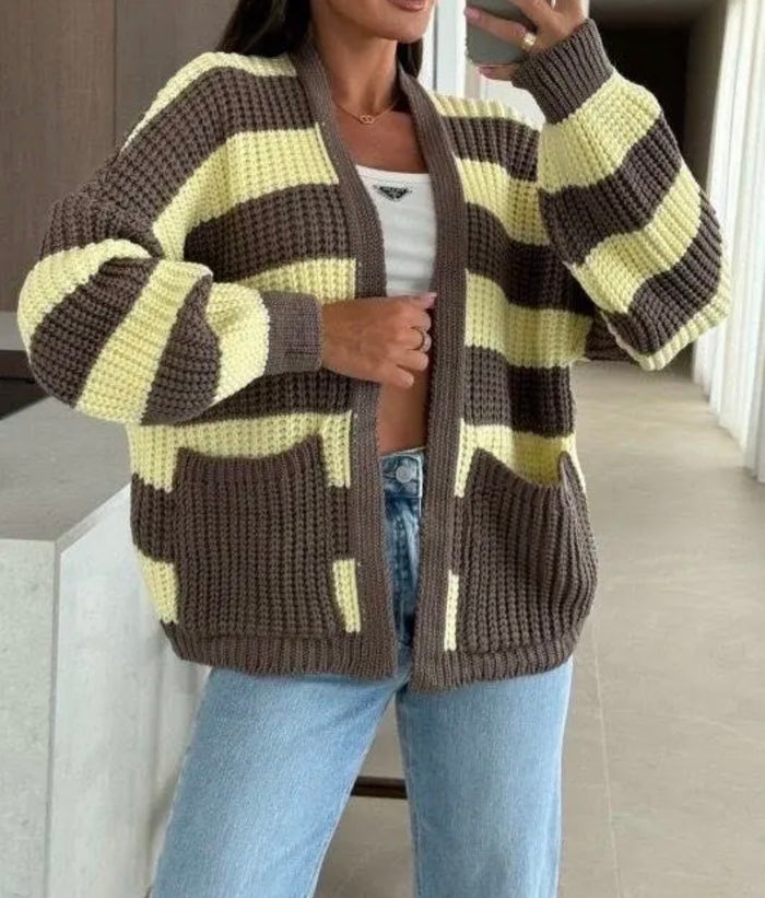 Person wearing a brown and yellow Noeleen Stripe Cardigan with blue jeans indoors.