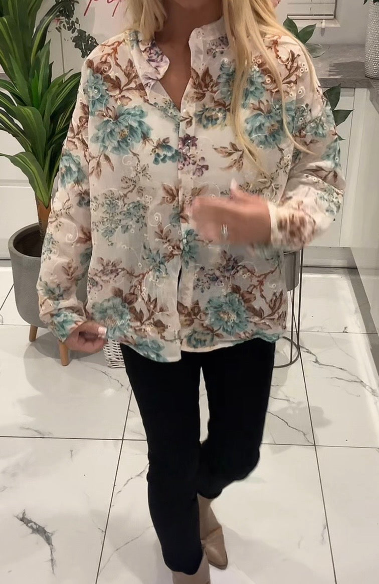 Person wearing a floral blouse and black pants in an indoor setting with plants.