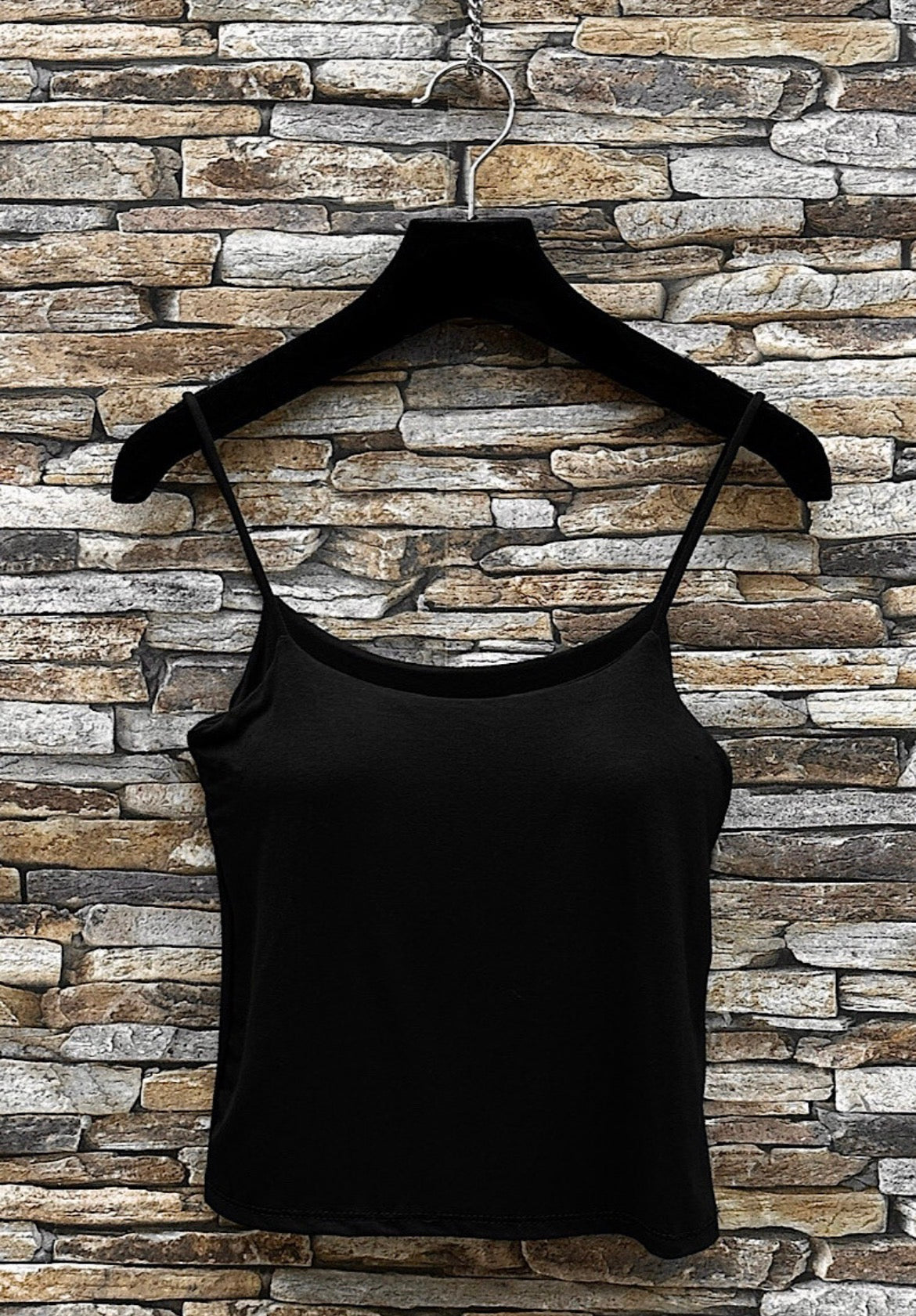 Black tank top on a hanger against a stone wall background