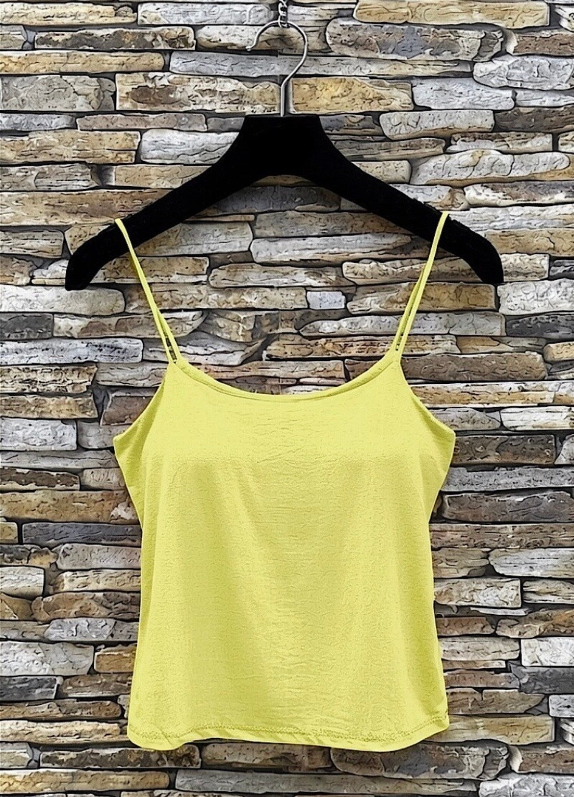 Yellow tank top on a black hanger against a stone wall background