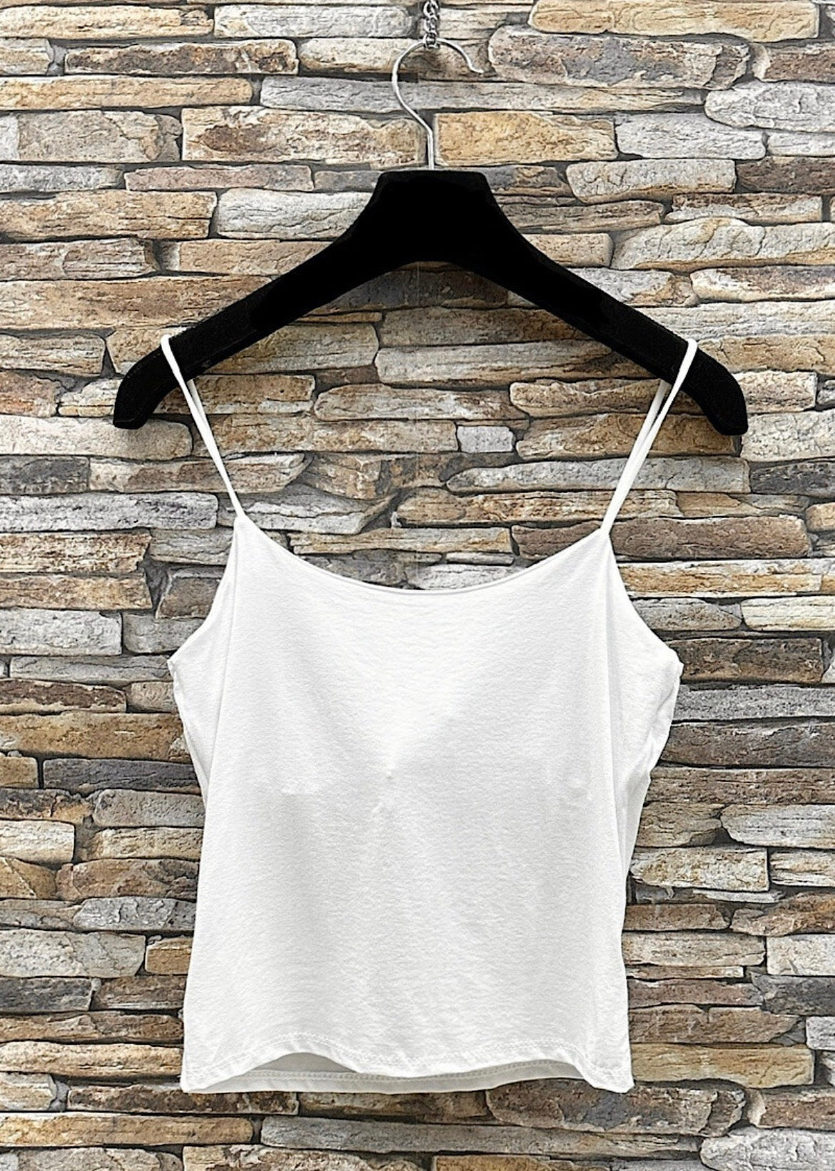 White spaghetti strap top on a black hanger against a stone wall background