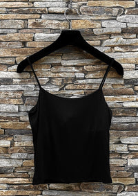 Black spaghetti strap top on a hanger against a stone wall background