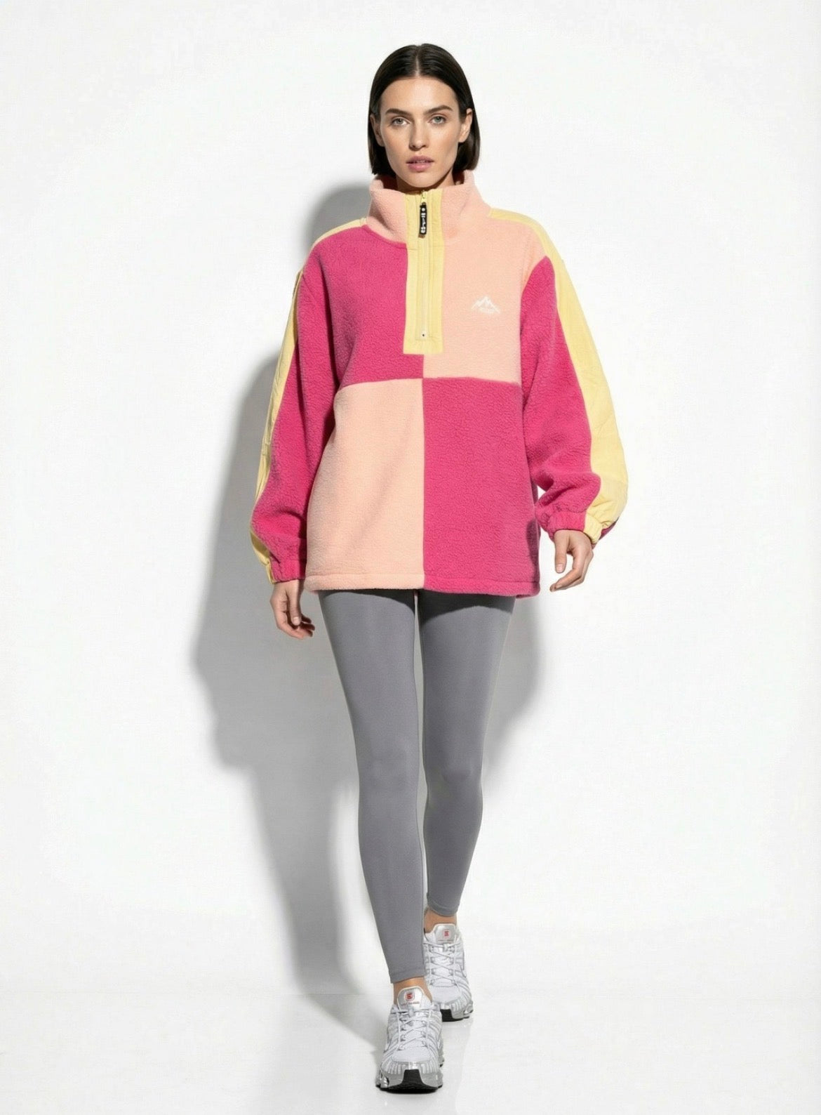 Person wearing a colorful checkered sweater and gray leggings on a white background