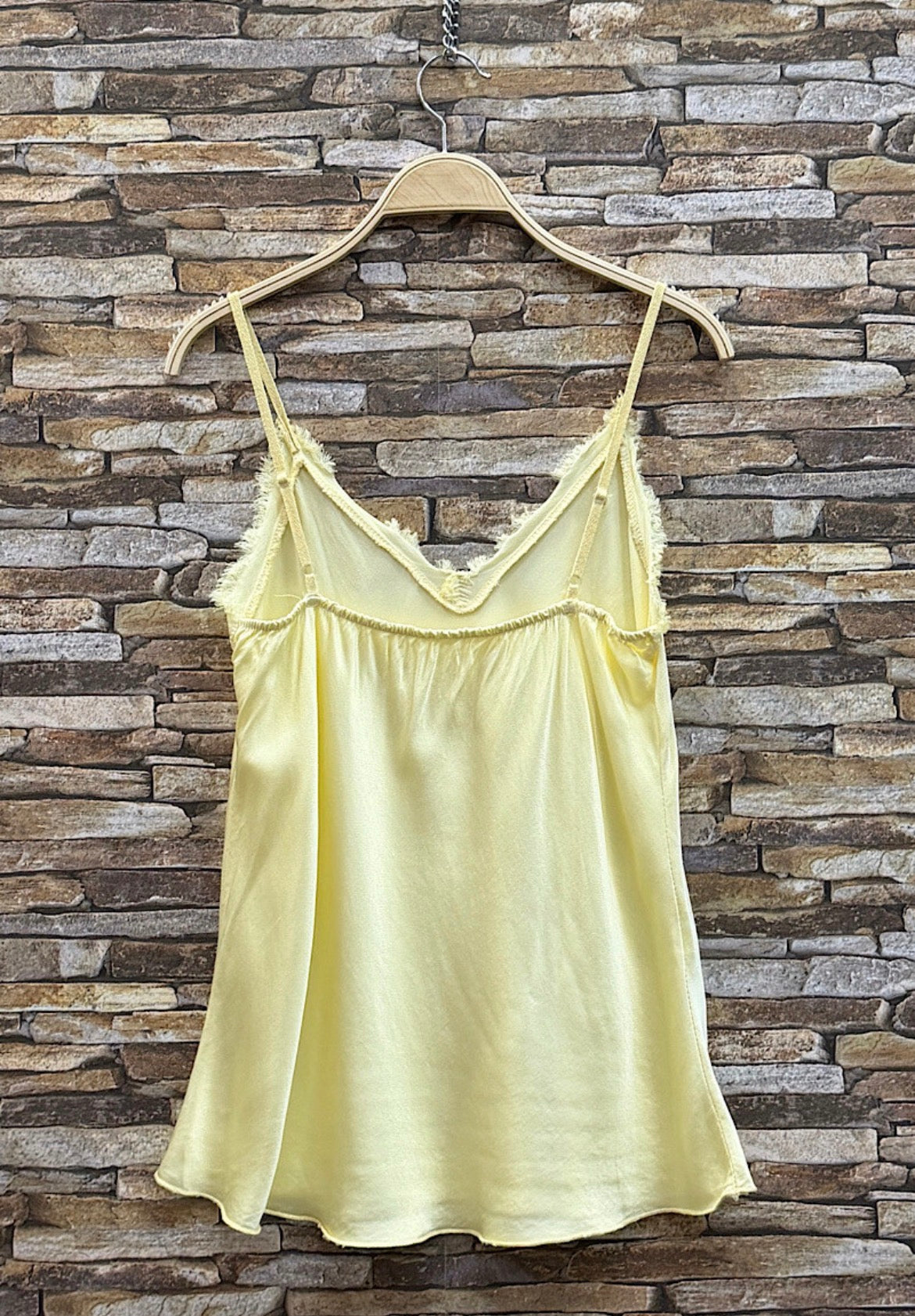 Yellow satin camisole on a hanger against a stone wall background