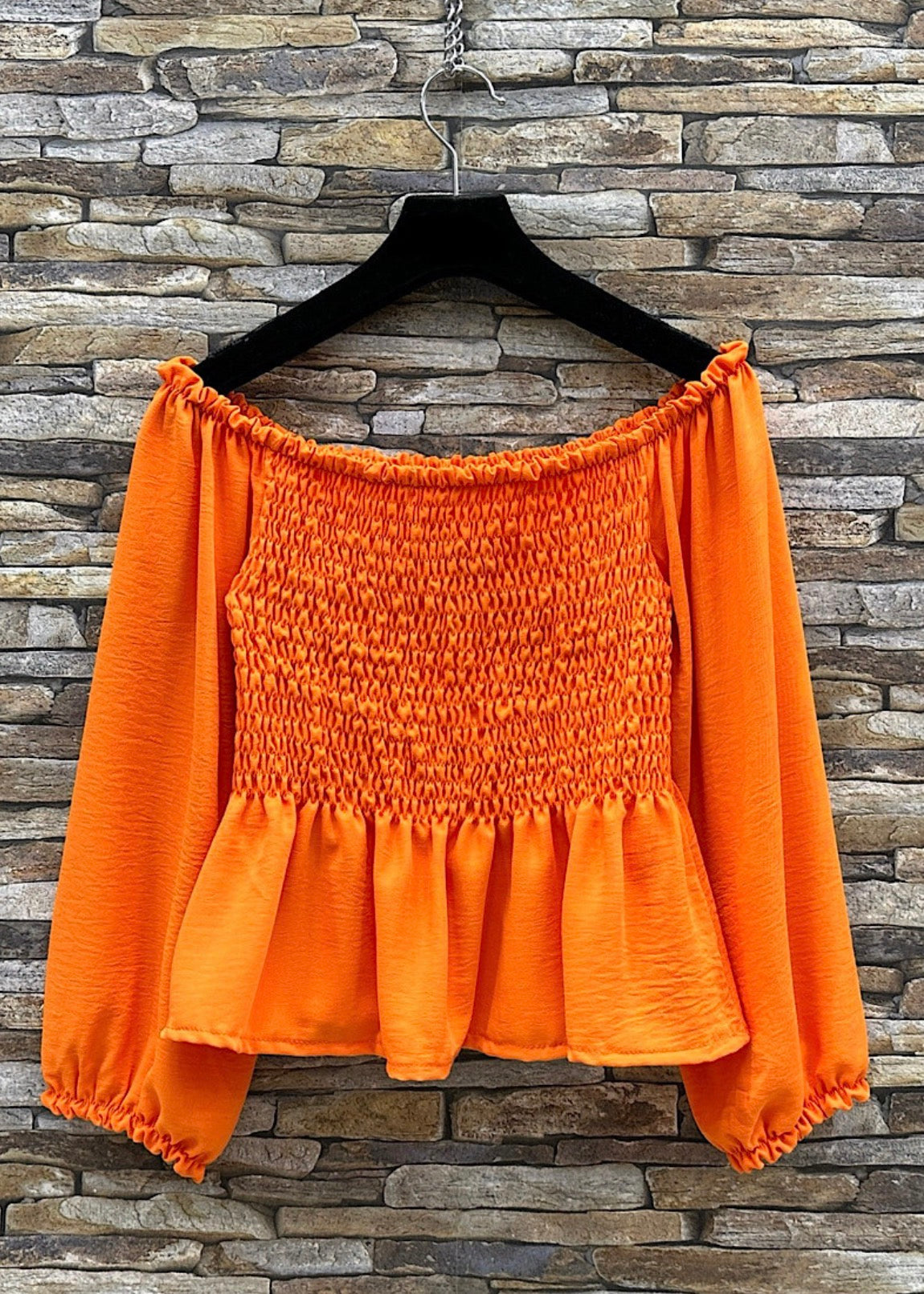 Orange off-shoulder top on a hanger against a stone wall background
