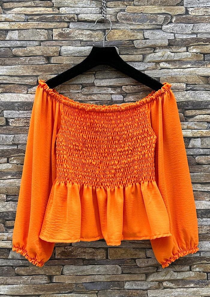 Orange off-shoulder top on a hanger against a stone wall background