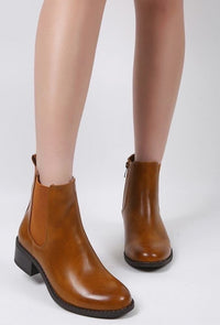 Brown leather ankle boots worn by a person on a white background