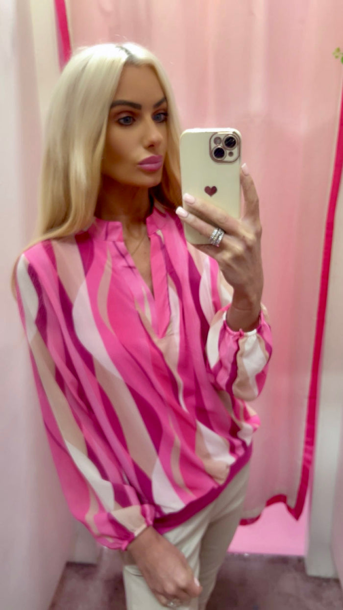 Woman taking a mirror selfie wearing a pink and white striped shirt against a pink curtain.