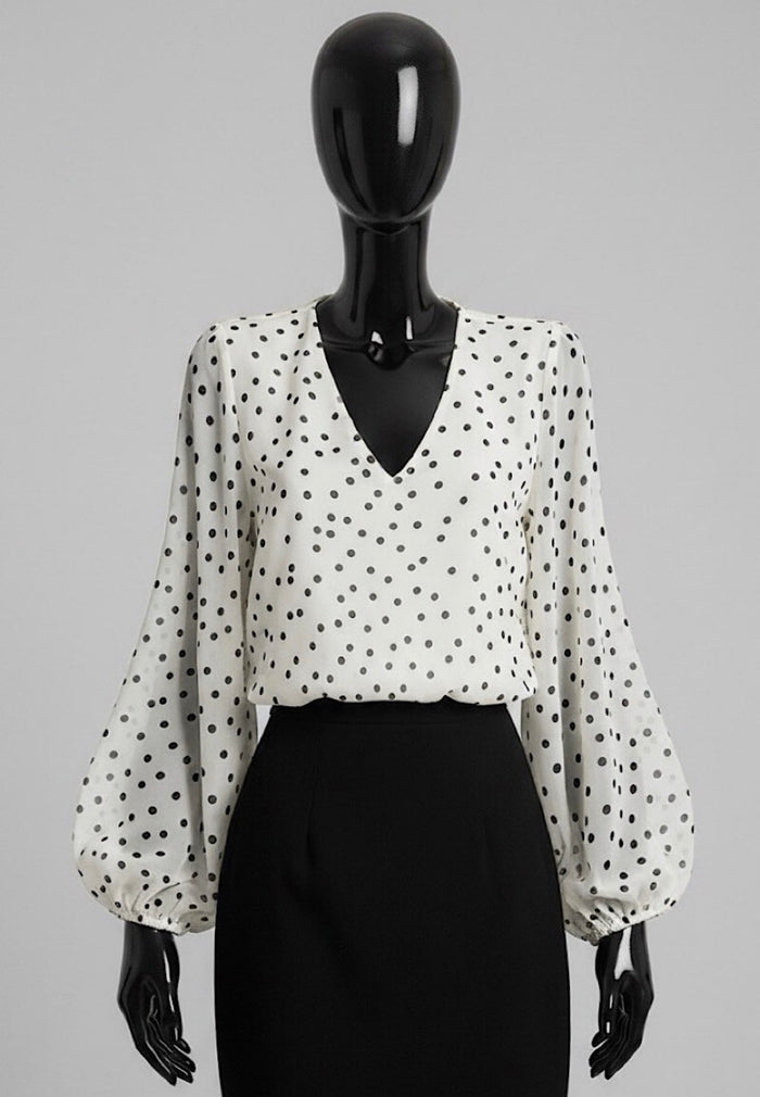 A black and white polka dot blouse with balloon sleeves and a V-neckline, displayed on a black mannequin torso against a solid gray background.