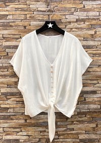 White blouse with buttons on a hanger against a stone wall background