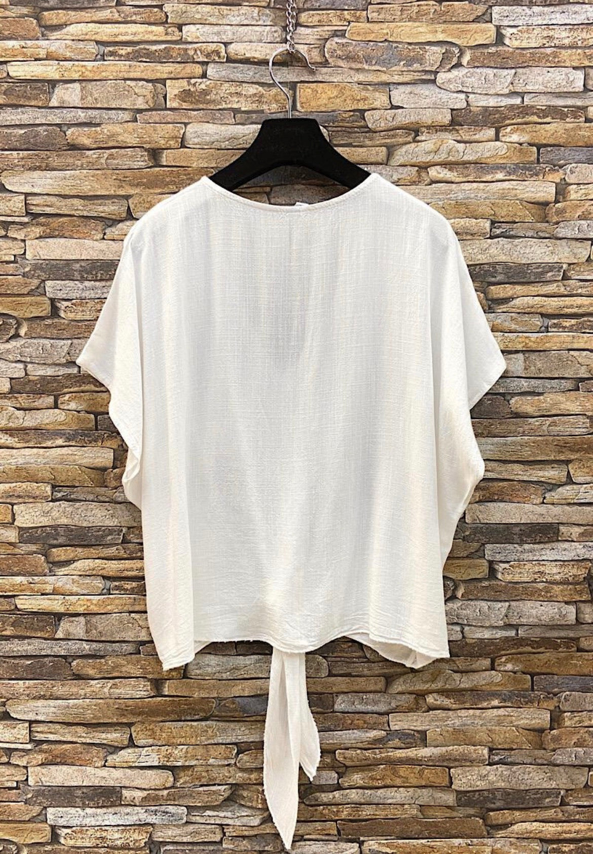 White blouse with a tie detail on a hanger against a stone wall background