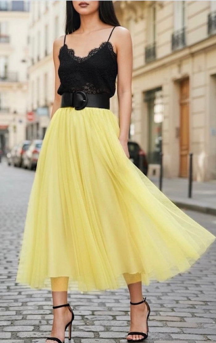 Woman wearing a black lace top and yellow skirt on a city street.