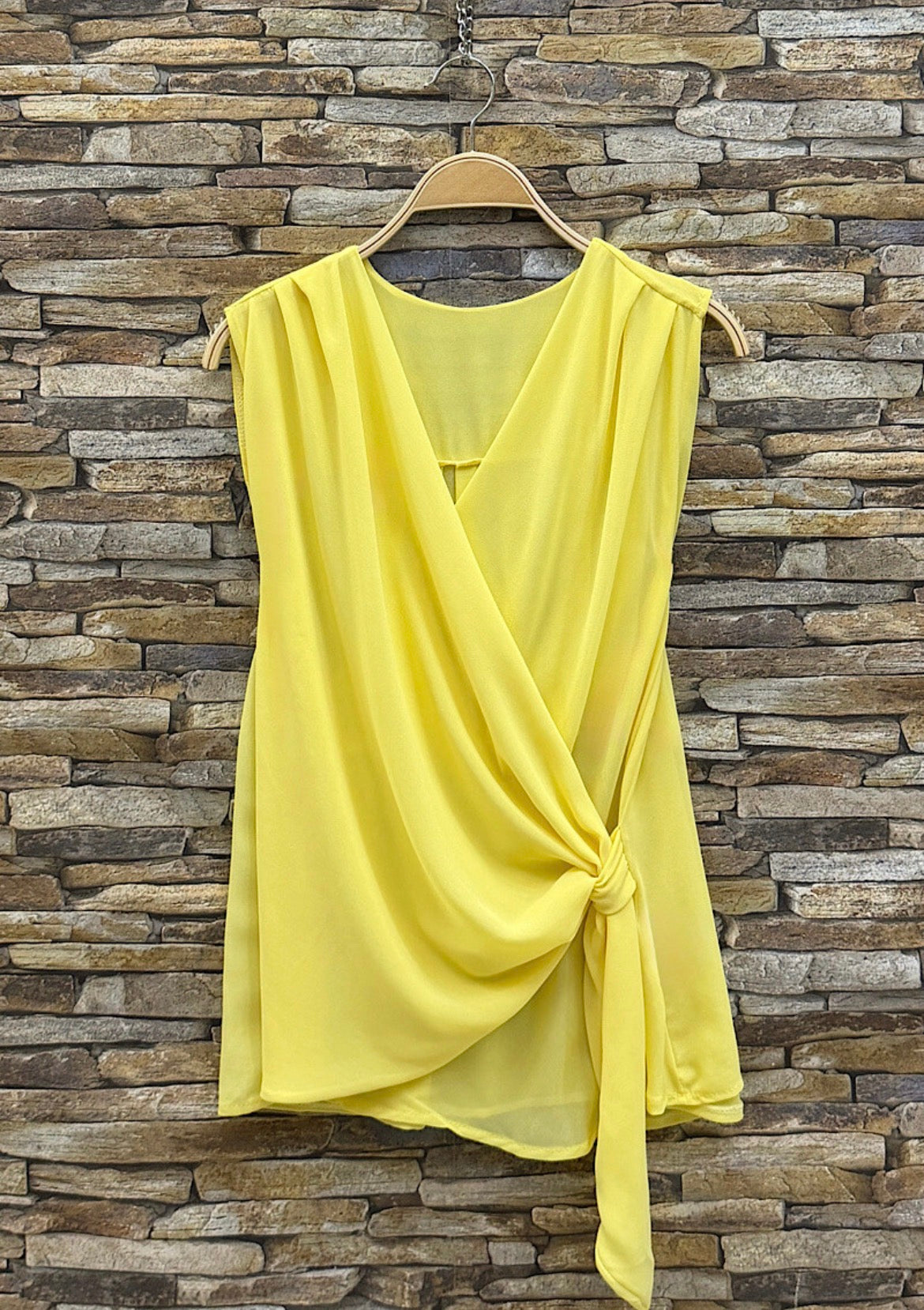 Yellow sleeveless top on a hanger against a stone wall background