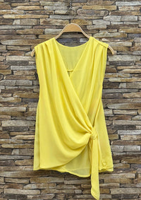 Yellow sleeveless top on a hanger against a stone wall background