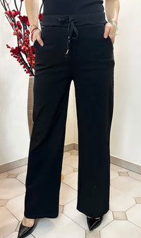 Person wearing black high-waisted pants with a white wall and decorative plant in the background