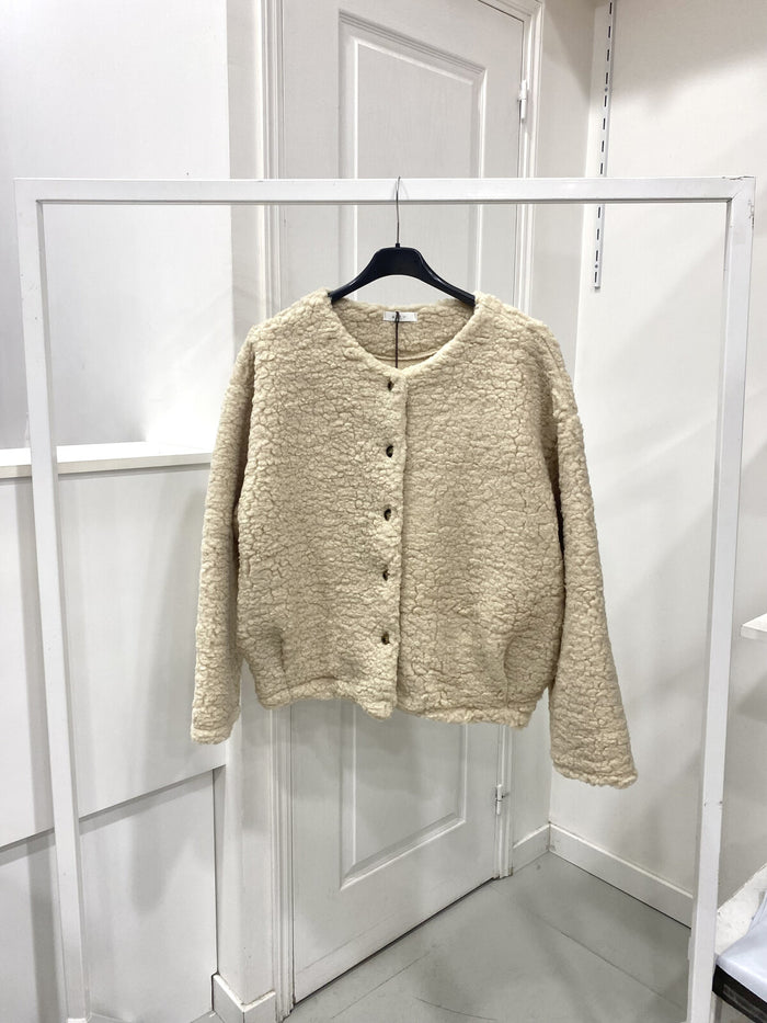 Beige cardigan on a hanger against a white wall "Zita Teddy Jacket – Cosy Statement Outerwea"